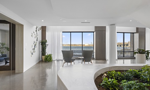 Serene Lounge with Panoramic Waterfront Views at Gibson Point Modern indoor lounge at Gibson Point featuring two armchairs facing large windows with scenic waterfront views, surrounded by lush indoor plants and natural light.